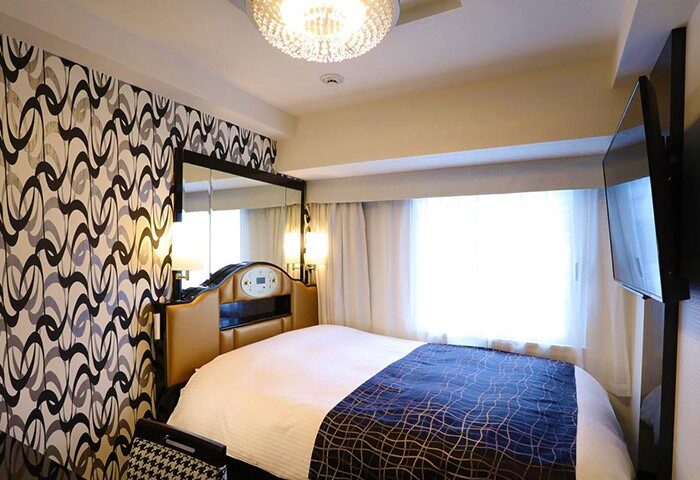 APA HOTEL Shinjuku Kabukicho Chuo room. Gay-friendly hotel with double bed, patterned wallpaper, TV, and modern lighting. Tokyo travel lodging.