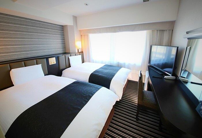 APA Hotel Shinjuku-Gyoemmae gay-friendly room. Twin beds, desk, and TV. Modern decor, clean lines. A comfortable stay in Tokyo's vibrant Shinjuku.