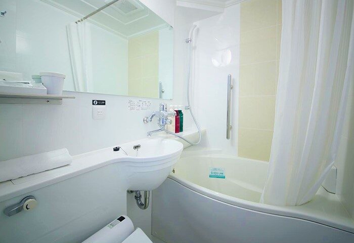 APA Hotel Shinjuku-Gyoemmae bathroom. Clean, well-lit space with a sink, mirror, and bathtub with shower. Gay-friendly hotel in Tokyo.