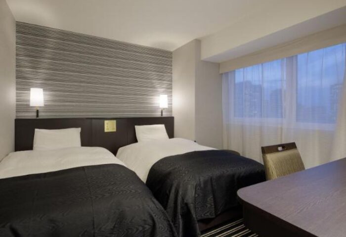 Twin beds in APA Hotel Shinjuku-Kabukicho Tower, a gay-friendly hotel. Modern room with desk, chair, and window. Tokyo travel advice.