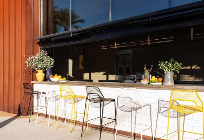 ARRIVE Palm Springs gay-friendly hotel outdoor bar. Colorful stools line the counter with fruit and flowers. A cool spot for gay travelers.