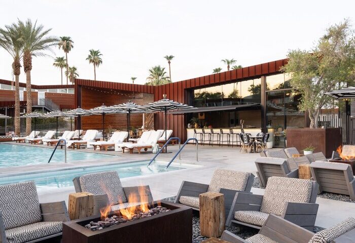Arrive Palm Springs gay-friendly hotel pool area with lounge chairs, umbrellas, fire pit, and bar. Perfect for gay travel and relaxation.
