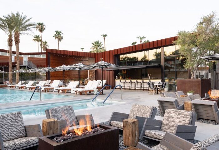 Arrive Palm Springs gay-friendly hotel pool area with lounge chairs, umbrellas, fire pit, and bar. Perfect for gay travel and relaxation.