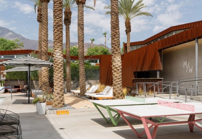 ARRIVE Palm Springs gay-friendly hotel outdoor space. Ping pong tables, lounge chairs, palm trees, and mountain views. Gay travel advice.