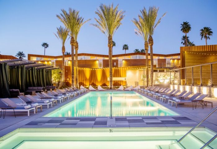 ARRIVE Palm Springs hotel pool at dusk. Gay-friendly hotel with palm trees, lounge chairs, and modern design. Perfect for gay travel in Palm Springs.