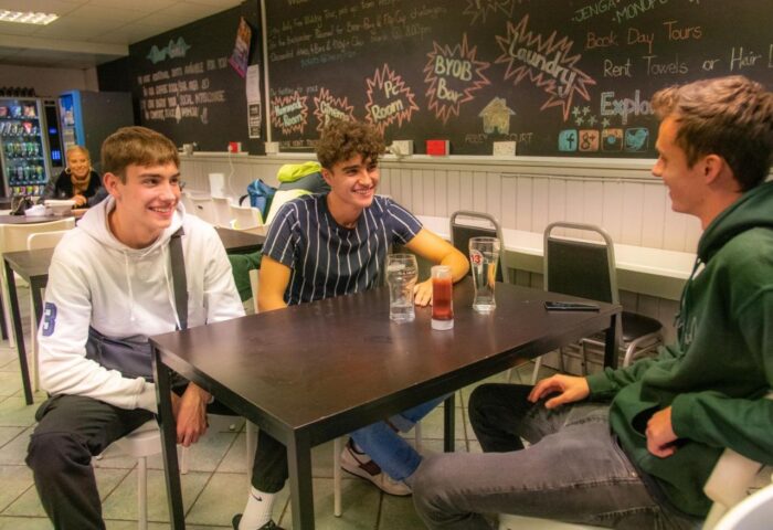 Gay-friendly Abbey Court Hostel: Three young men chatting at a table, enjoying drinks. A relaxed atmosphere for gay travelers. Socializing at the hostel.