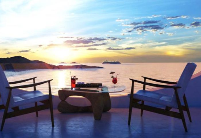 Mykonos sunset view from Absolute Mykonos Suites & More, a gay-friendly hotel. Cocktails on table, chairs, sea, cruise ship. Perfect gay travel.