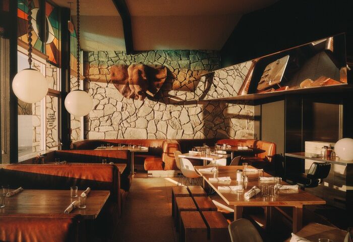 Ace Hotel Palm Springs restaurant. Retro interior, stone wall, leather booths, and globe lights. Gay-friendly hotel dining.