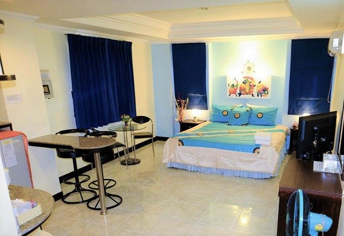 Adonis Guest House room. Gay-friendly hotel with a blue bedspread, matching pillows, and dark blue curtains. A table and chairs are visible.