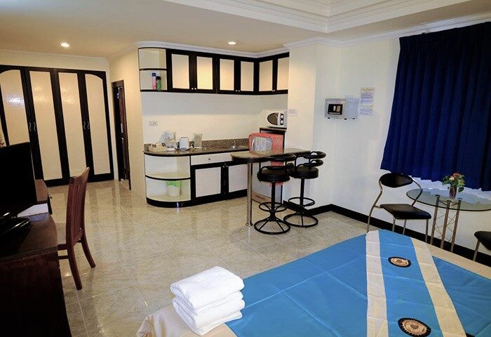 Adonis Guest House gay-friendly hotel room interior. Kitchenette, bar stools, and bed with blue and white bedding. Modern design.