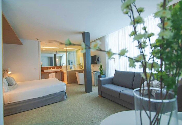 Alenti Sitges Hotel room interior. Gay-friendly hotel featuring a bed, sofa, and bathroom with a tub. Modern design for gay men travelers.