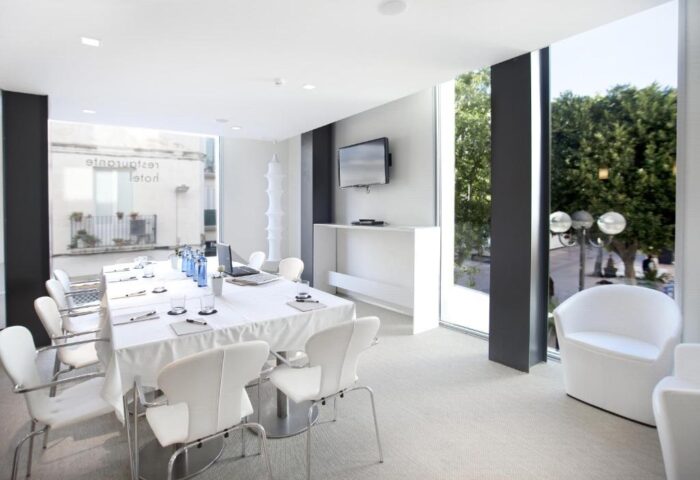 Alenti Sitges Hotel & Restaurant meeting room. Gay-friendly hotel with white table, chairs, and large windows. Modern design for business or leisure.