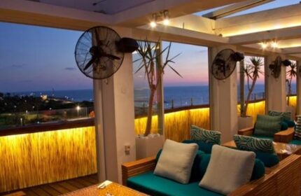 Alexander Tel Aviv Hotel's gay-friendly terrace at dusk. Sea view seating area with fans, plants, and cozy cushions. Perfect for gay travelers.