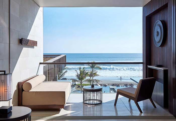Alila Seminyak, a gay-friendly hotel. Balcony view of the ocean, palm trees, and beach. Relaxing travel destination for gay men.