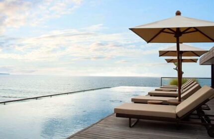 Alila Seminyak gay-friendly hotel: infinity pool with ocean view. Loungers and umbrellas on wooden deck. Ideal for gay men travel advice.