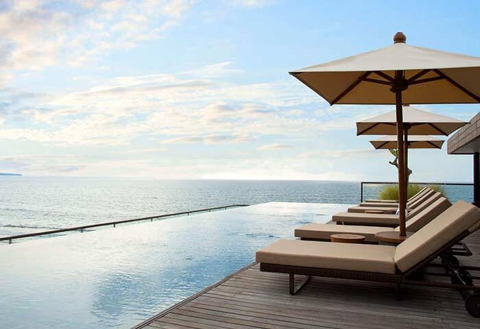 Alila Seminyak gay-friendly hotel: infinity pool with ocean view. Loungers and umbrellas on wooden deck. Ideal for gay men travel advice.