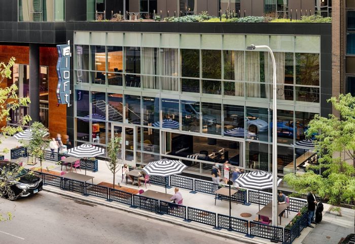 Aloft Chicago Mag Mile's exterior. Gay-friendly hotel with outdoor seating under striped umbrellas. Modern design, street view.