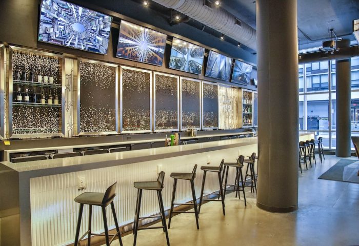 Bar area at the gay-friendly Aloft Chicago Mag Mile hotel. Modern design, stools, and screens above the bar. Great spot for gay travelers.