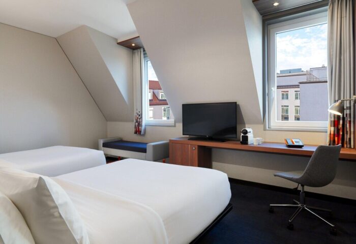 Aloft Munich hotel room. Gay-friendly hotel with twin beds, desk, TV, & city view. Modern design, comfortable stay. Munich travel advice.