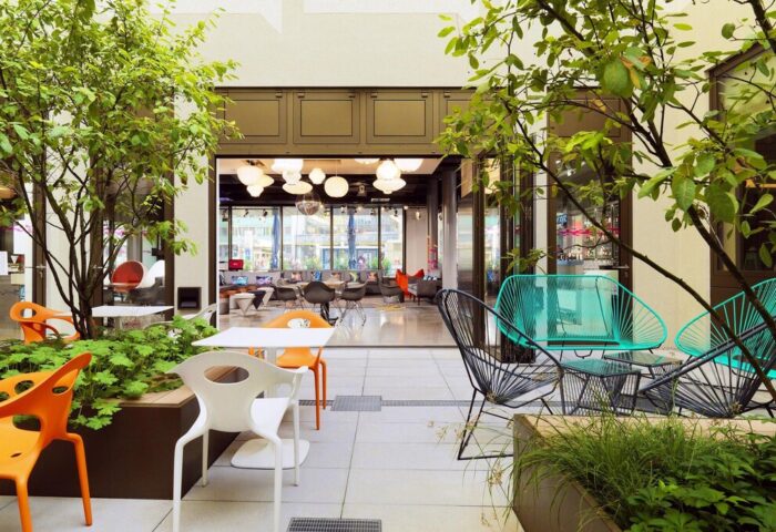 Aloft Munich hotel courtyard. Outdoor seating area with colorful chairs and tables. Gay-friendly hotel with modern design elements.