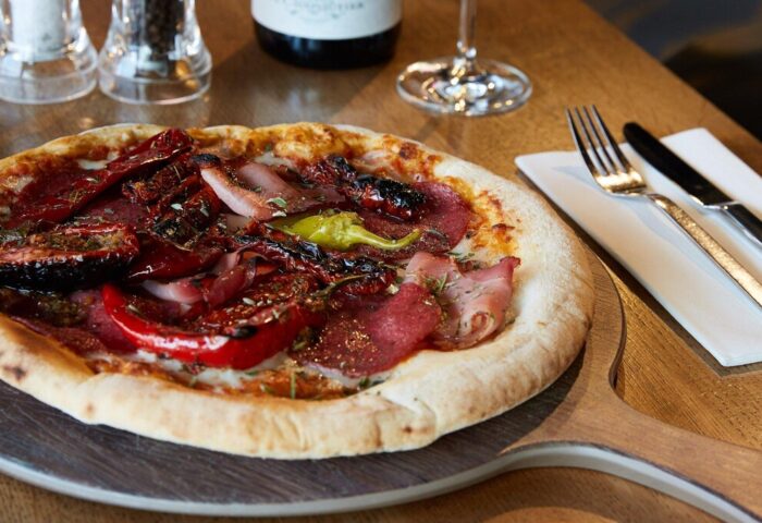 Pizza at Aloft Munich, a gay-friendly hotel. Delicious meal with peppers, salami, and herbs on a wooden board. Fine dining in Munich.