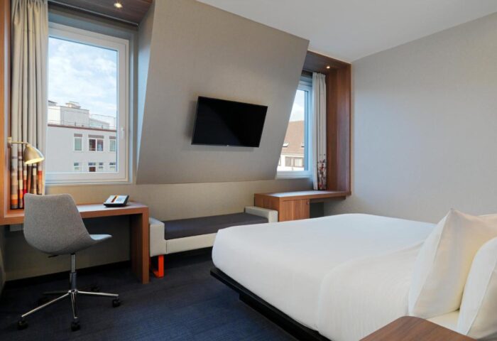 Aloft Munich room. Gay-friendly hotel with desk, chair, TV, and bed. Modern design, comfortable for LGBTQ+ travelers. Munich hotel room.