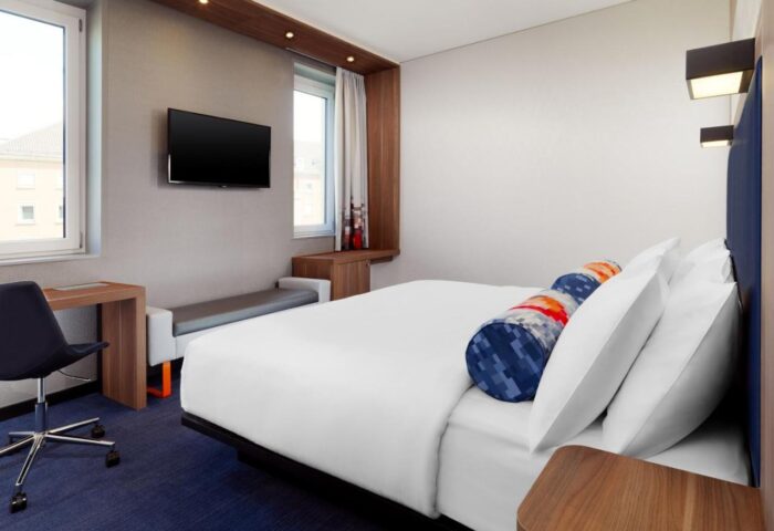 Aloft Munich room. Gay-friendly hotel with modern decor, bed with white linens, desk, and TV. Perfect for gay travelers in Munich.