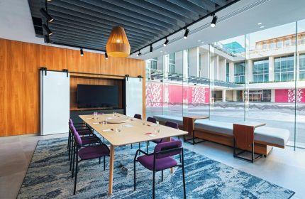 Aloft Playa del Carmen gay-friendly hotel meeting room. Table with purple chairs, TV, and large windows. Modern design for LGBTQ+ travelers.