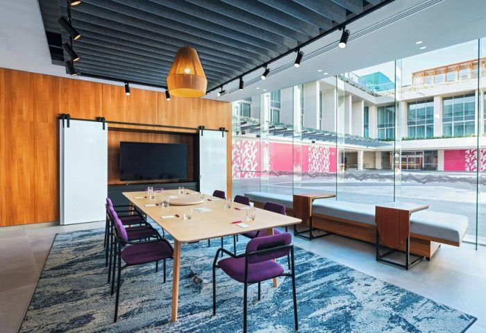 Aloft Playa del Carmen gay-friendly hotel meeting room. Table with purple chairs, TV, and large windows. Modern design for LGBTQ+ travelers.