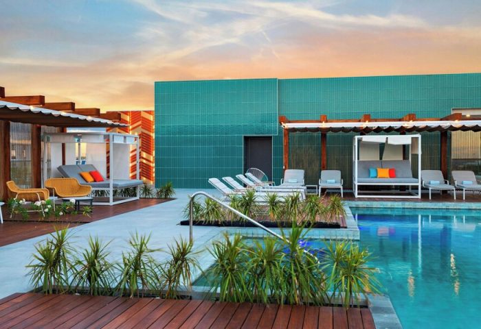 Rooftop pool at Aloft Playa del Carmen, a gay-friendly hotel. Loungers, daybeds, and vibrant decor create a stylish, welcoming atmosphere.