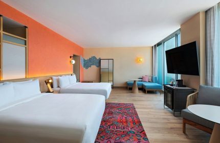 Aloft Playa del Carmen gay-friendly hotel room. Two beds, colorful decor, and a seating area. Modern design for gay travelers.