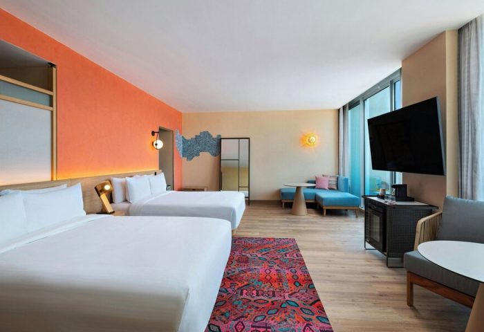 Aloft Playa del Carmen gay-friendly hotel room. Two beds, colorful decor, and a seating area. Modern design for gay travelers.