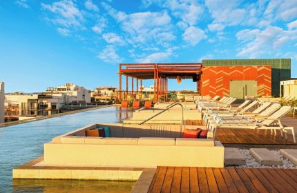 Rooftop pool at Aloft Playa del Carmen, a gay-friendly hotel. Lounge chairs, colorful pillows, and blue sky create a relaxing vibe.