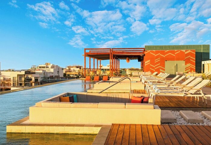 Rooftop pool at Aloft Playa del Carmen, a gay-friendly hotel. Lounge chairs, colorful pillows, and blue sky create a relaxing vibe.