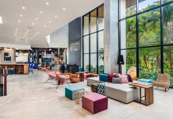 Aloft Tulum's stylish lobby. This gay-friendly hotel features modern decor, floor-to-ceiling windows with jungle views, and colorful seating areas.