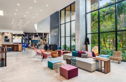 Aloft Tulum's stylish lobby. This gay-friendly hotel features modern decor, floor-to-ceiling windows with jungle views, and colorful seating areas.