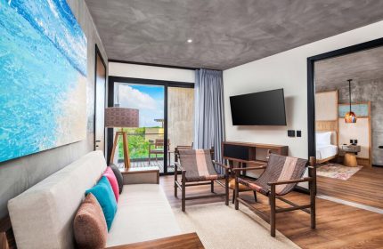Aloft Tulum gay-friendly hotel room showcasing modern decor, stylish seating, a balcony with lush views, and a glimpse into the bedroom.