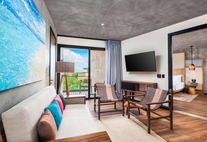 Aloft Tulum gay-friendly hotel room showcasing modern decor, stylish seating, a balcony with lush views, and a glimpse into the bedroom.
