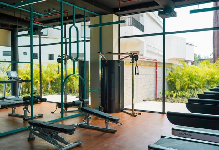 Aloft Tulum gay-friendly hotel gym. Treadmills, weight machines, and benches face large windows overlooking lush greenery. Fitness center.