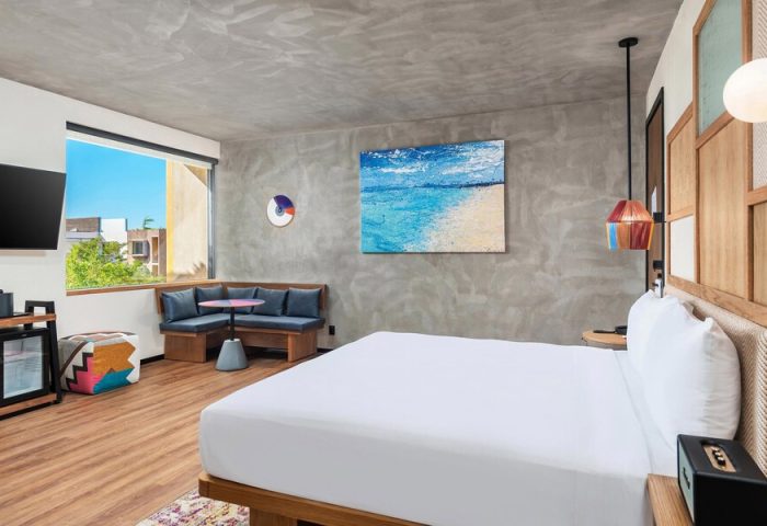 Aloft Tulum hotel room. Gay-friendly hotel with modern decor, white linens, and a seating area. Beach painting on the wall. Perfect for gay travel.