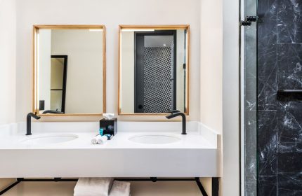 Aloft Tulum gay-friendly hotel bathroom. Double vanity with mirrors, black fixtures, white countertop, and towels. Shower with black marble tiles.