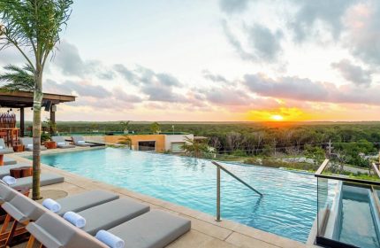 Aloft Tulum gay-friendly hotel infinity pool at sunset. Loungers and a bar area are visible. A great place for gay men to travel and relax.