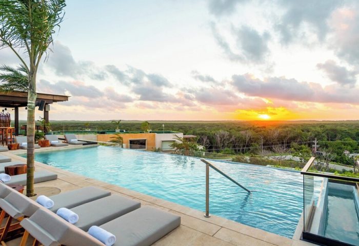 Aloft Tulum gay-friendly hotel infinity pool at sunset. Loungers and a bar area are visible. A great place for gay men to travel and relax.