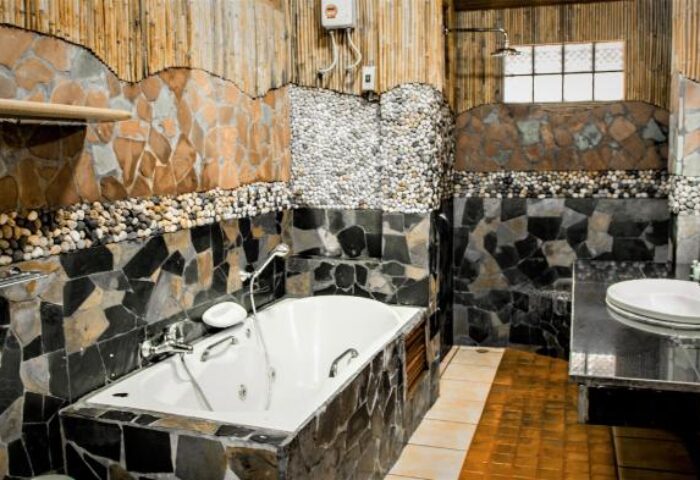 Bathroom at Alpha Gay Resort & Spa, a gay men only, pet-friendly hotel. Features a stone-tiled tub and walls, plus a shower.