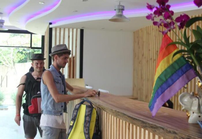 Guests checking in at Alpha Gay Resort & Spa, a gay men-only, pet-friendly hotel. Rainbow flag visible. Gay-Friendly hotel welcome.