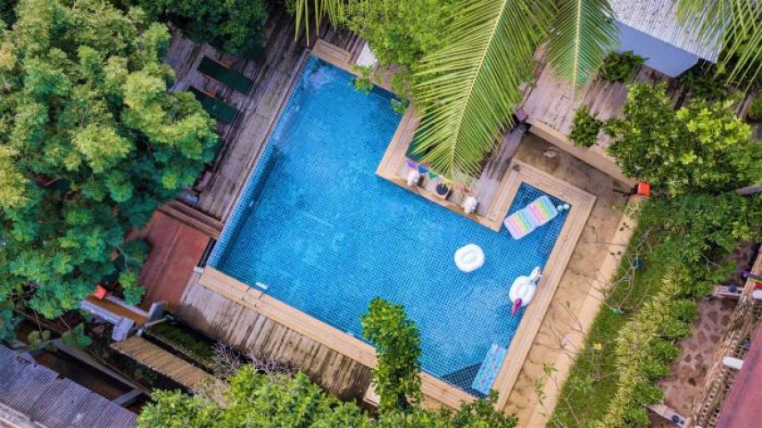Aerial view of Alpha Gay Resort & Spa, a gay men only, pet-friendly hotel. Blue pool with inflatables, surrounded by lush greenery.