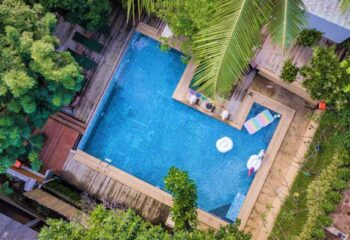 Aerial view of Alpha Gay Resort & Spa, a gay men only, pet-friendly hotel. Blue pool with inflatables, surrounded by lush greenery.