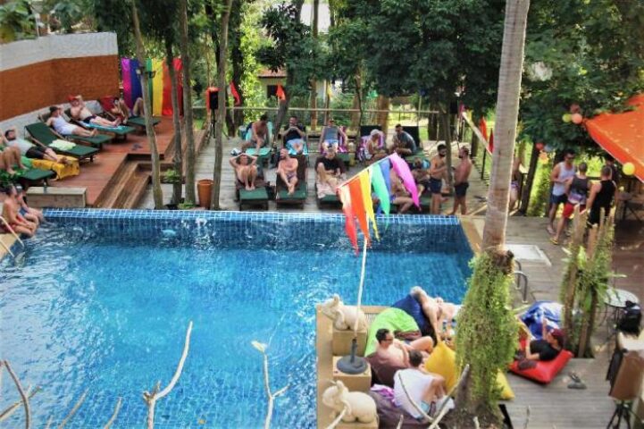 Alpha Gay Resort & Spa pool view. Gay men relaxing at a pet-friendly, gay-friendly hotel. Tropical spa with rainbow flags. Gay travel.