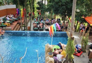 Alpha Gay Resort & Spa pool view. Gay men relaxing at a pet-friendly, gay-friendly hotel. Tropical spa with rainbow flags. Gay travel.