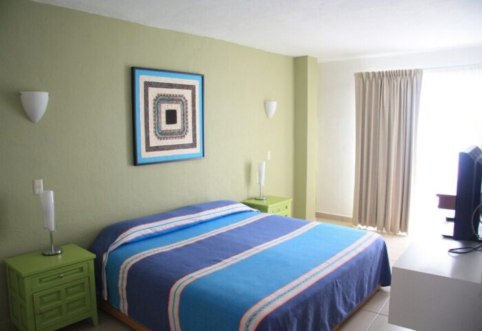 Amapas Apartments Puerto Vallarta gay-friendly hotel room. Blue striped bed, green nightstands, and modern art. Comfortable stay for gay travelers.